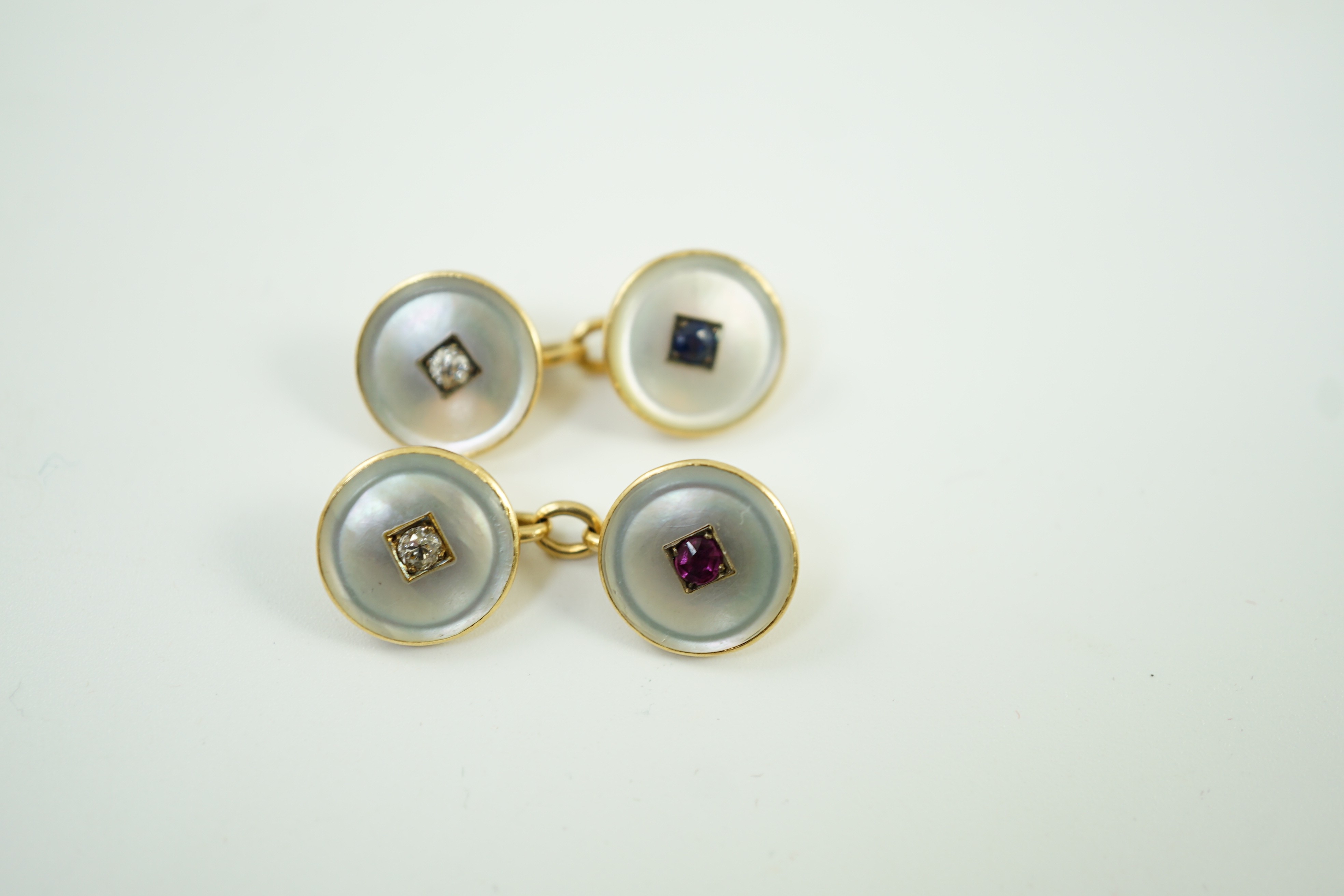 A pair of early to mid 20th century yellow metal mounted mother of pearl and gem set cufflinks, one set with a ruby and diamond, the other with a sapphire and diamond, link diameter 12mm, gross weight 8 grams.